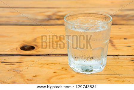 Glass water with iceDrops water on glass placed on wooden table.