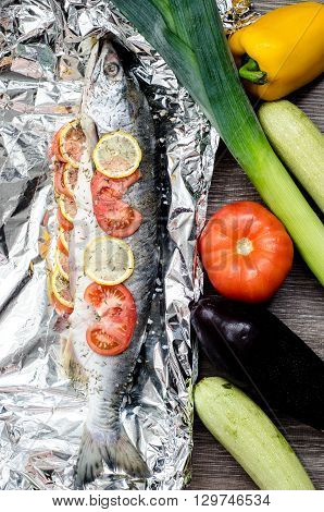Salmon with lemon and tomatoes on the foil ready to bake with vegetables