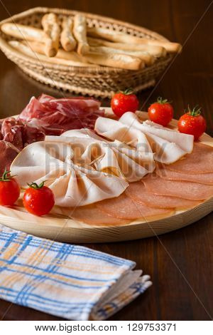 Salami cutting board cherry tomatoes breadsticks on a wicker basket and a napkin