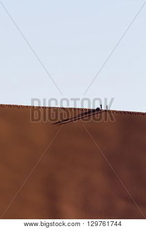 People walking on the crest of a red dune in the Namib Desert in Sossusvlei in the Namib-Naukluft National Park of Namibia