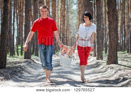 Happy family with child in backet walking at bright summer day