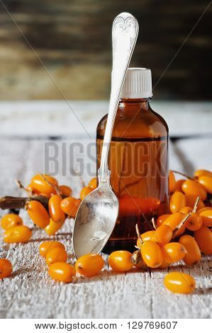 Sea buckthorn oil in a bottle and fresh sea buckthorn on a white wooden background. Alternative medicine. Selective focus