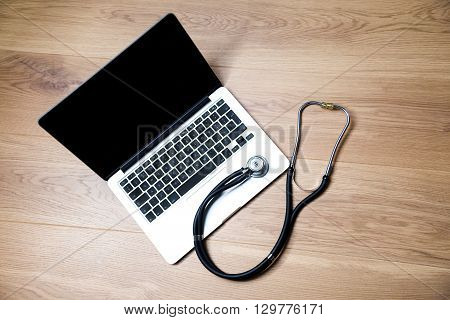 Top view of notebook with blank screen and stethscope next to it on wooden desktop. Mock up