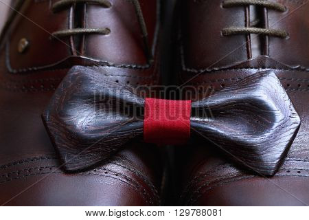 Wooden bow tie with red ribbon on the leather male shoes.