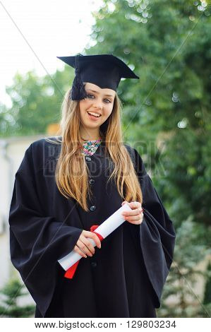 The young girl holding diploma. She is dressed in cap and gown. In the face of a beautiful smile