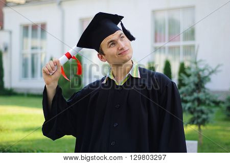 The young man with a diploma in hand and black robe looks at the sky