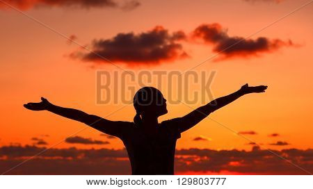 Woman's silhouette on sunset light, happy girl with raised up hands standing on the beach and enjoying warm summer evening, doing yoga exercise outdoors