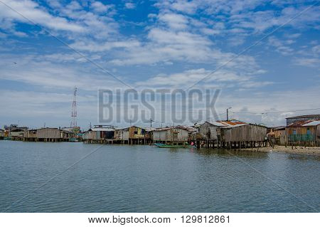 Muisne, Ecuador - March 16, 2016: Muisne town as seen from water, modest wooden houses sitting on poles waterfront pacific ocean, city buildings background and beautiful blue sky.