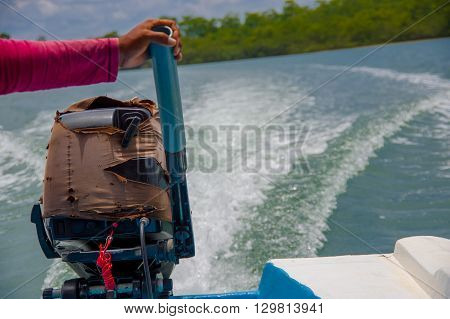 Muisne, Ecuador - March 16, 2016: Arm holding onto boat engine, wave trace visible on water from driving, great perspective and beautiful colours.