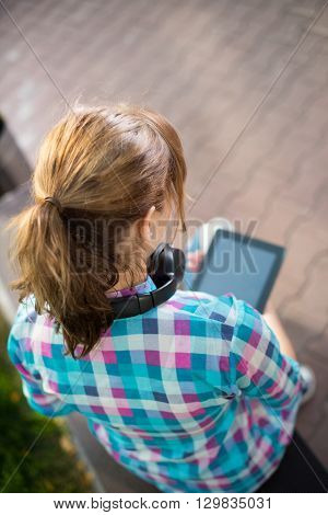 Preparing to exams outdoors. Beautiful young female student writing or reading something from note pad.  Woman sitting on bench in city park.