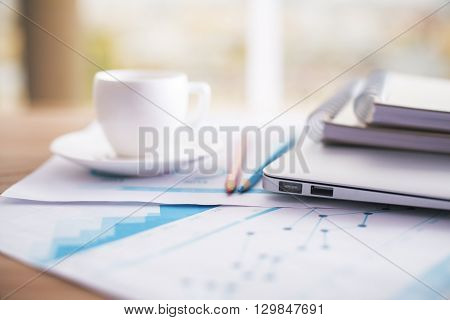 Closeup of coffee cup business review pencils notepads and laptop on office desktop