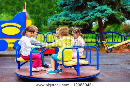 Group Of Happy Kids Having Fun On Roundabout At Playground