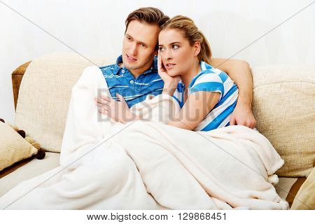 Smiling loving couple sitting on couch with blanket
