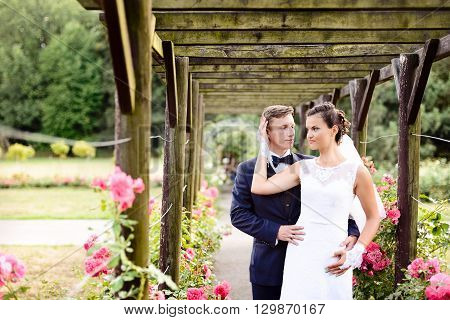Newlyweds In Park Rosarium Next To Beautiful Pink Roses