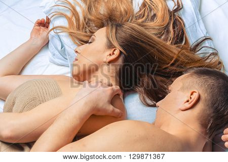 Young couple lying in bed. She is sleeping. Her hair scattered on the pillow. Selective focus on woman's face.