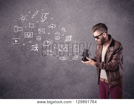 An elegant hipster guy trying to use a vintage camera with camera settings icons drawn on wall, like flash, white balace or ISO value concept