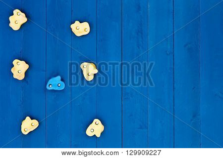 Top down view on seven oddly shaped yellow and blue climbing grip handholds on wooden wall with copy space