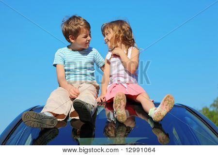 liten pojke och flicka sitter på biltaket på blå himmel, talar
