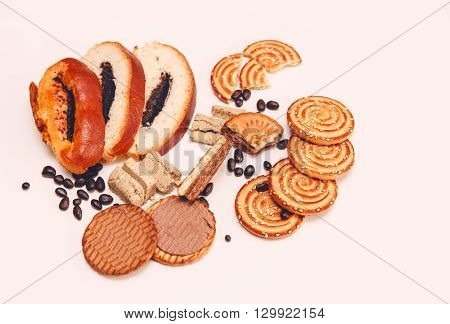 There are Pieces of Roll with Poppy seed,Cookies and Halavah,Chocolate PeasTasty Sweet Food on the White Background,Top View,Toned