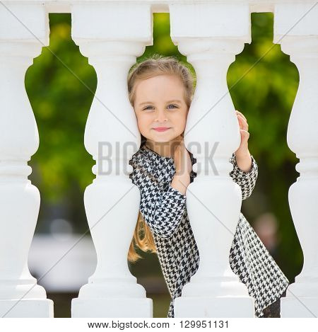 Little beautiful girl hiding behind balister on the summer street