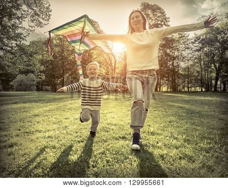 Runnings little boy and mother flies with them kite in the park under sunligt.