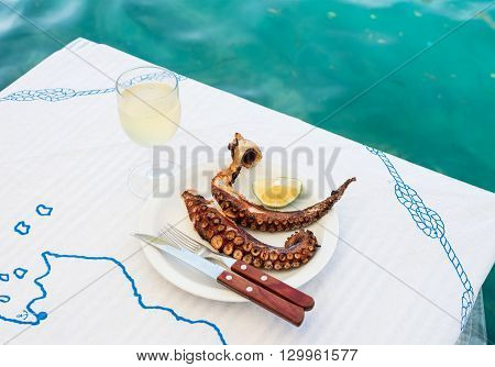 Grilled octopus and white wine glass on a table at the sea coast in small restaurant on a Greek island of Kastelorizo