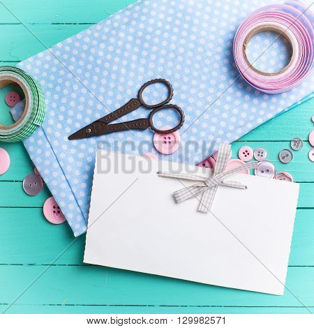 Sewing thread - buttons scissors fabric and empty tag on turquoise wooden background. Selective focus. Scrapbboking. Flat lay. Place for text. Toned image.