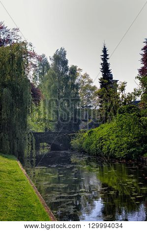 An old stone bridge leads over a tiny canal in a park at Bussum the Netherlands.