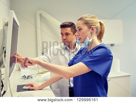 people, medicine, stomatology, technology and health care concept - dentists looking to x-ray scan on monitor at dental clinic