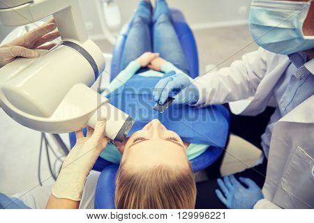 people, medicine, stomatology, technology and health care concept - close up of dentist putting intraoral shield to female patient mouth and assistant directing x-ray machine at dental clinic