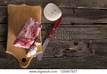 Piece of frozen meat onions and garlic. A table from old boards rural style