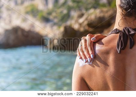 Woman Rubs Sunscreen On His Shoulder. Against The Background Of The Sea.
