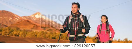 Hiking hikers couple trekking in nature mountains at sunset with walking poles and backpack wearing outdoor gear jackets. Happy multiracial group of friends, man and woman hiking banner panorama.