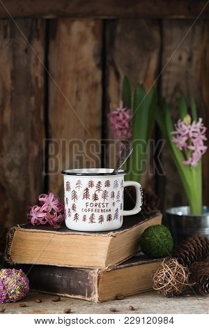 White Ceramic Cup Of Coffee On Old Books On Rustic Wooden Background With Cones And Hyacinth. Toned.