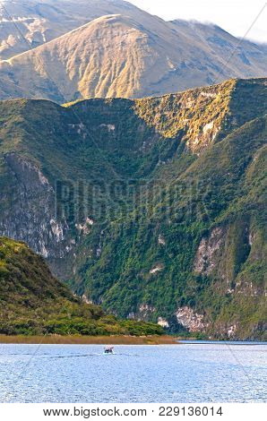 View Of The Cuicocha Lake And Crater, With A Small Touristic Boat In The Water, On A Sunny And Cloud