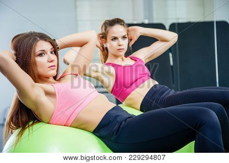 Two Young Women Doing Abdominal Exercises Using The Gymnastic Ball In A Gym