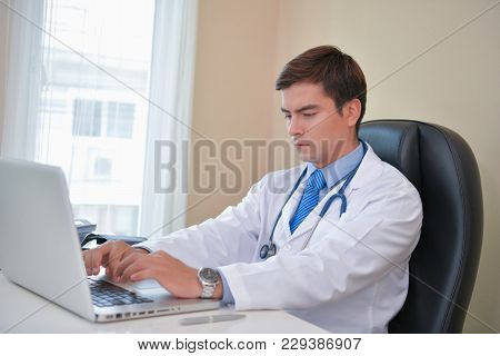 Smiling Doctor Posing In The Office, He Is Wearing A Stethoscope, Medical Staff On The Hospital Back