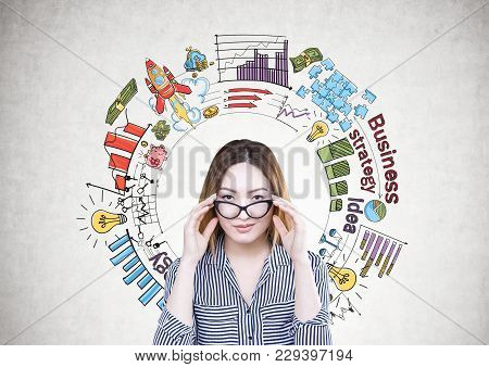 Attractive And Serious Asian Businesswoman Wearing A Striped Shirt Is Touching Her Glasses And Looki