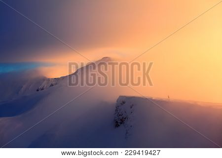 At The Edge Of The Snowy Rock Someone Is Standing. The High Mountains In The Fog, Morning Sky Is Enl