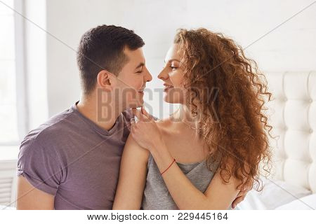 Portrait Of Affectionate Lovely Couple: Curly Woman And Brunet Male Look At Each Other`s Eyes With G