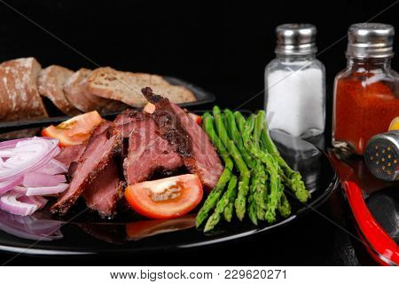 business lunch fresh roast beef meat slices on black plate wotj cutlery asparagus boiled broccoli rye bun on wooden table