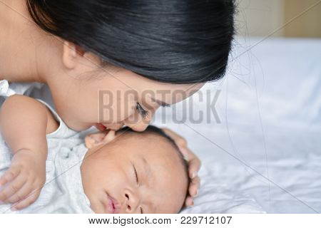 Newborn Concept. Mother And Child On A White Bed. Mom And Baby Boy Playing In Bedroom. Parent And Li