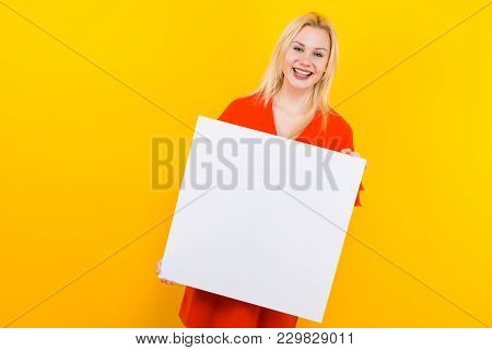 Portrait Of Attractive Happy Blonde Woman In Red Dress Isolated On Yellow Background Holding Emty Bl