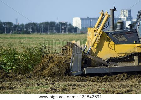 Russia, Temryuk - 15 July 2015: The Yellow Tractor With Attached Grederom Makes Ground Leveling. Wor