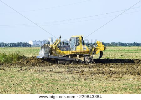 Russia, Temryuk - 15 July 2015: The Yellow Tractor With Attached Grederom Makes Ground Leveling. Wor