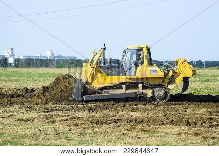 Russia, Temryuk - 15 July 2015: The Yellow Tractor With Attached Grederom Makes Ground Leveling. Wor