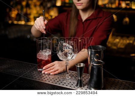 Barmen Girl Putting With A Tongs A Big Ice Cube Into An Empty Glass On The Steel Bar Counter