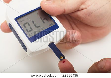 Man With Diabetes Using A Portable Digital Glucose Meter Drawing Up A Sample Of Blood From A Pinpric