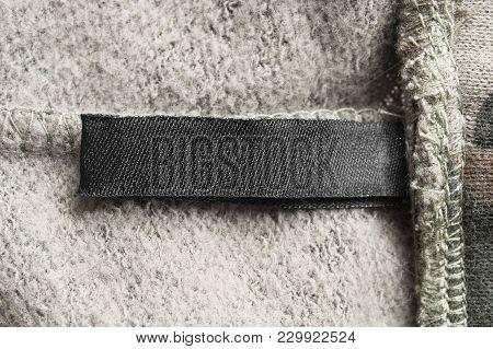 Blank Black Clothes Label On Beige Textile Background Closeup