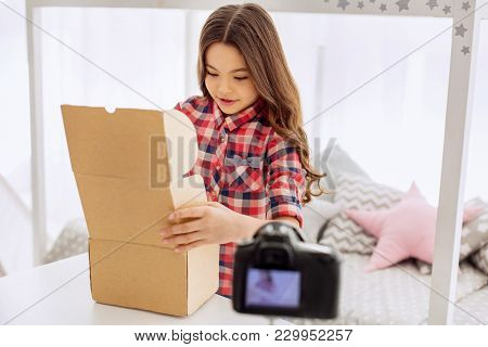 Curious Child. Petite Pre-teen Girl In A Checked Shirt Opening A Box And Looking Inside Curiously Wh
